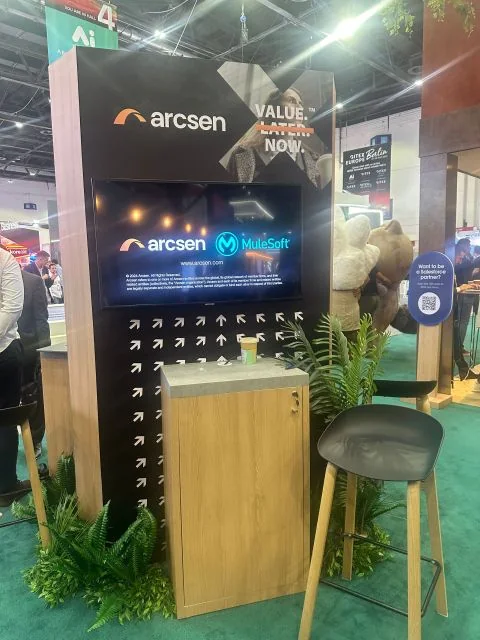 The Arcsen pod on the Salesforce stand at GITEX Global 2024, with the line Value, Later, Now and the word Later struck through, above a screen showing the Arcsen and MuleSoft logos