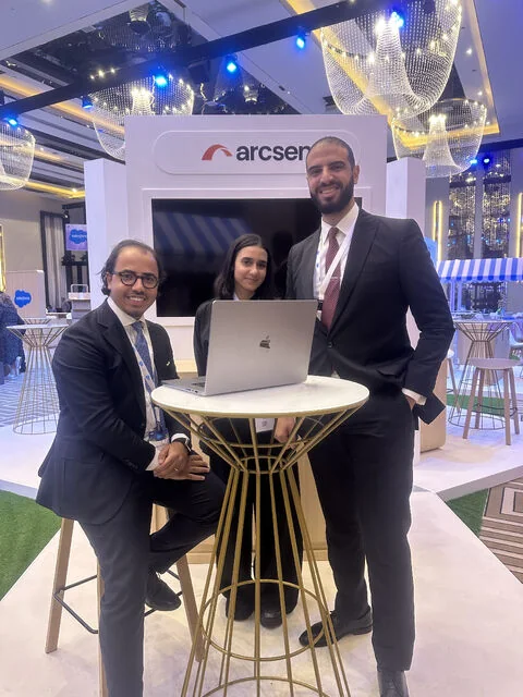 Three people at the white Arcsen booth, with a laptop on a high table, at Salesforce Innovation Day Riyadh 2025