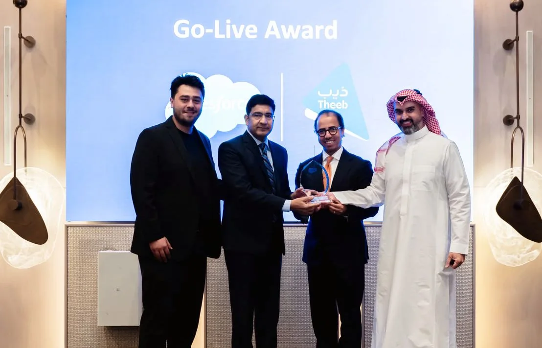 Four people on stage holding a glass award in front of a Go-Live Award screen showing the Salesforce and Theeb logos